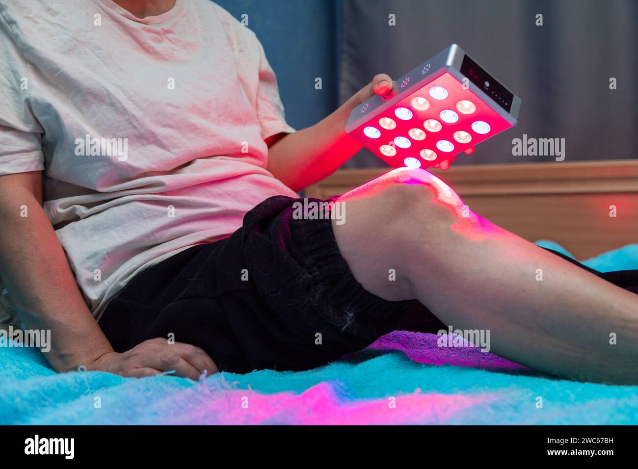 Gros plan sur le traitement des douleurs de jambe avec l'appareil portable de luminothérapie rouge à domicile sur le lit Banque D'Images