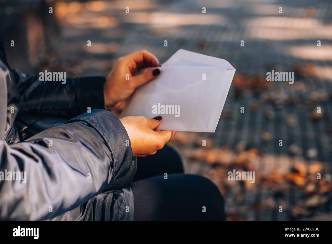 Femme ouvre une enveloppe blanche avec une lettre. Feuillage d'automne en arrière-plan. Banque D'Images