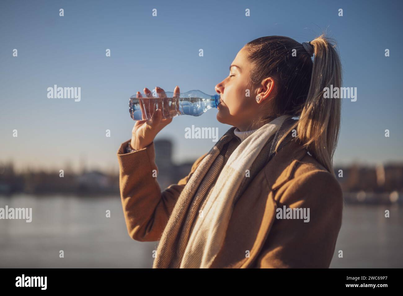 Femme aime boire de l'eau tout en étant assis au bord de la rivière sur une journée ensoleillée d'hiver. Image teintée. Banque D'Images