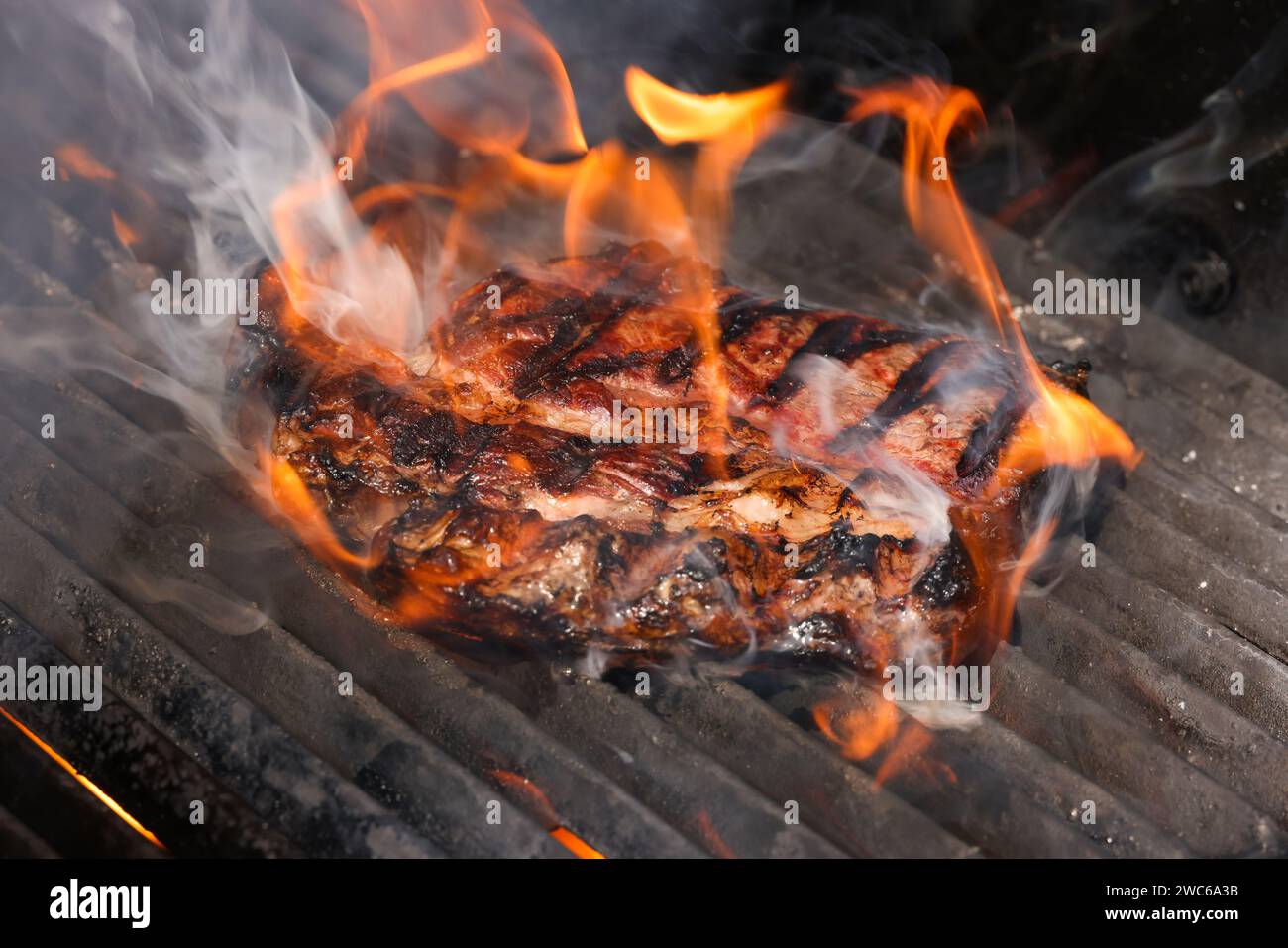 Gros plan sur des steaks de bœuf à la rivée et fumant sur une grille extérieure à feu ouvert avec grille en fonte métallique, vue en grand angle Banque D'Images