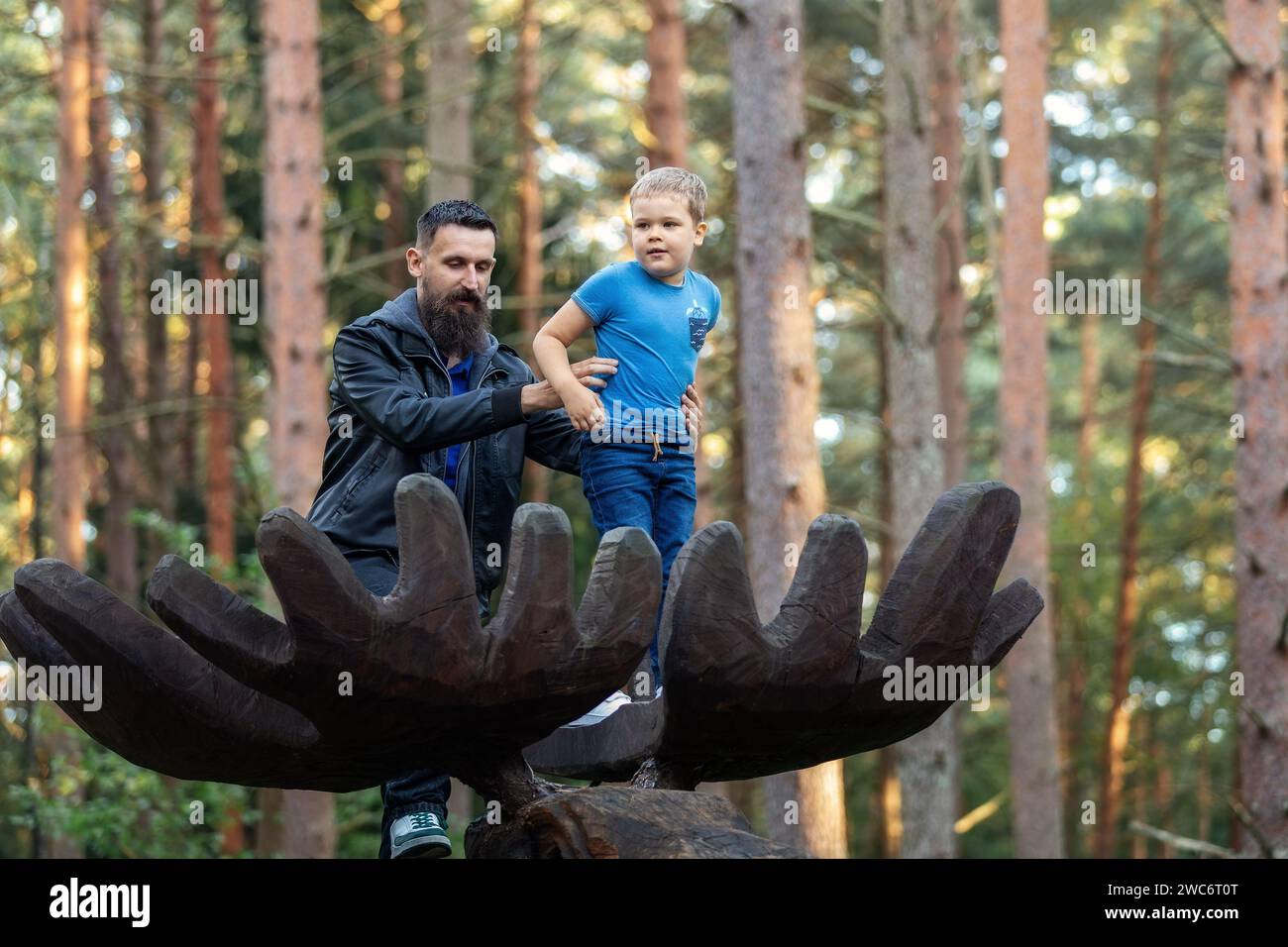 Portrait à faible angle en hauteur père et fils sur de grands bois d'élan en bois dans la forêt. Un père tient fermement son enfant pour qu'il ne tombe pas. Banque D'Images