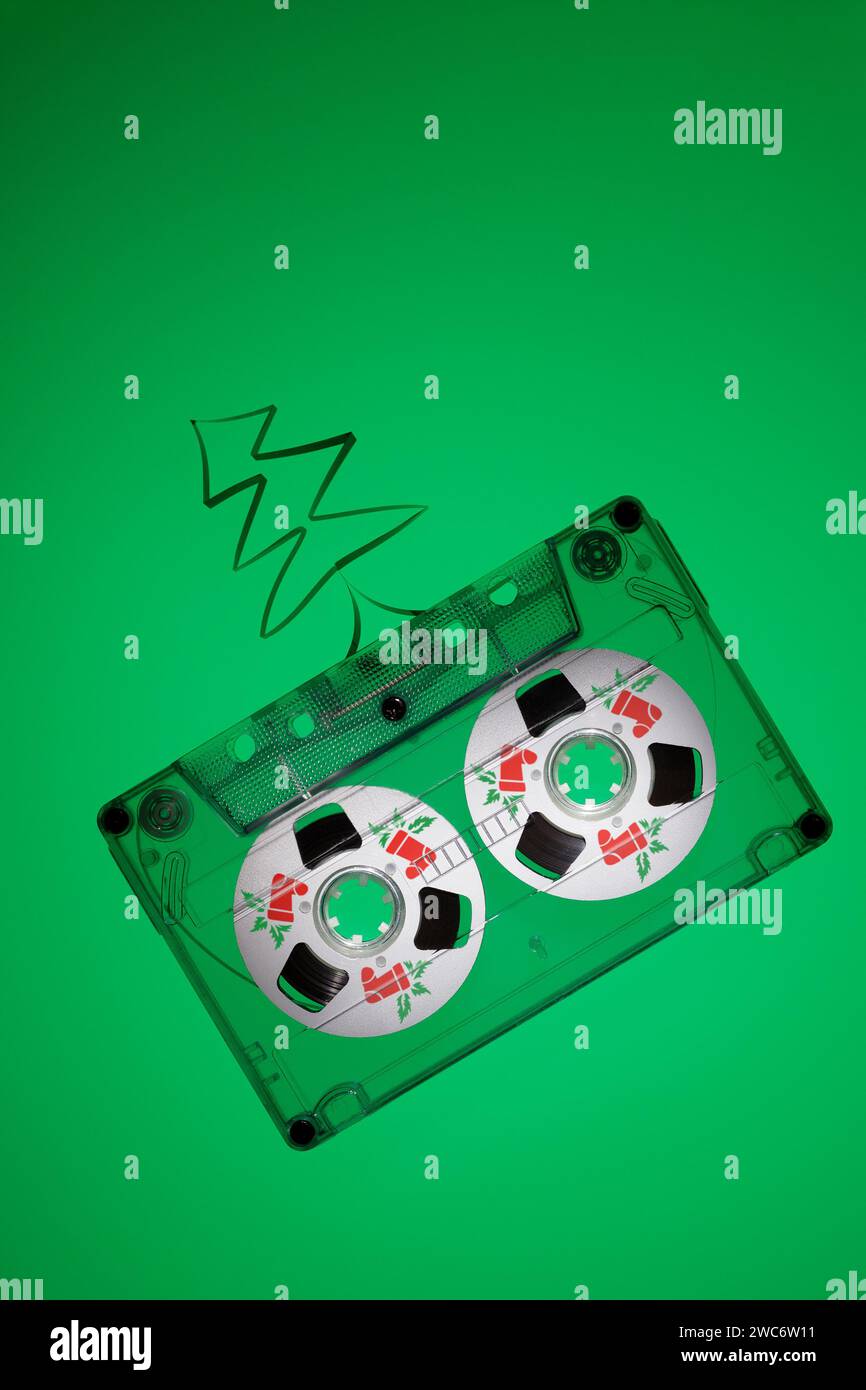 Photo verticale avec une cassette audio transparente sur fond vert éclairé par le bas. Carte musicale avec espace libre pour le texte sur le thème de Noël. Rouge p Banque D'Images