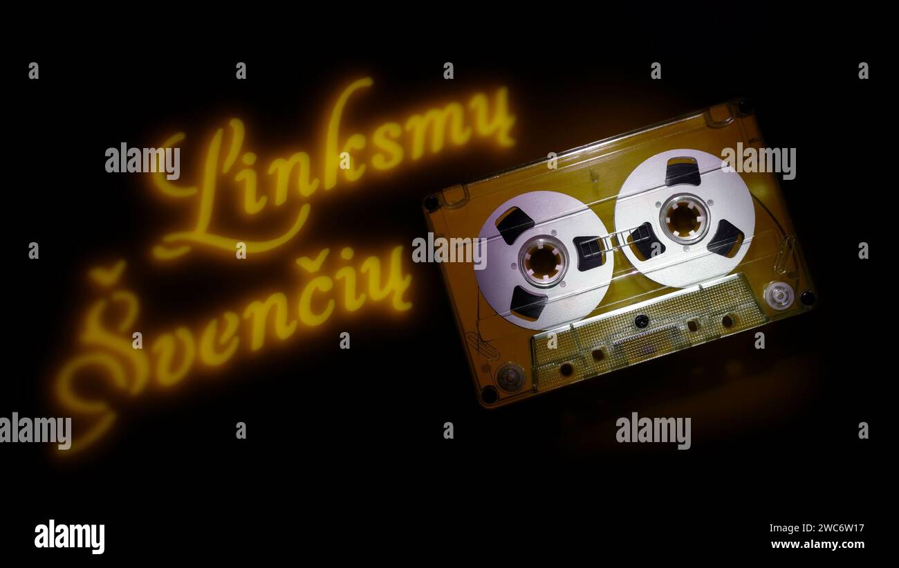 Carte, avec cassette audio transparente et projection de texte clair jaune - Joyeuses fêtes (texte en lituanien) sur fond sombre. Banque D'Images