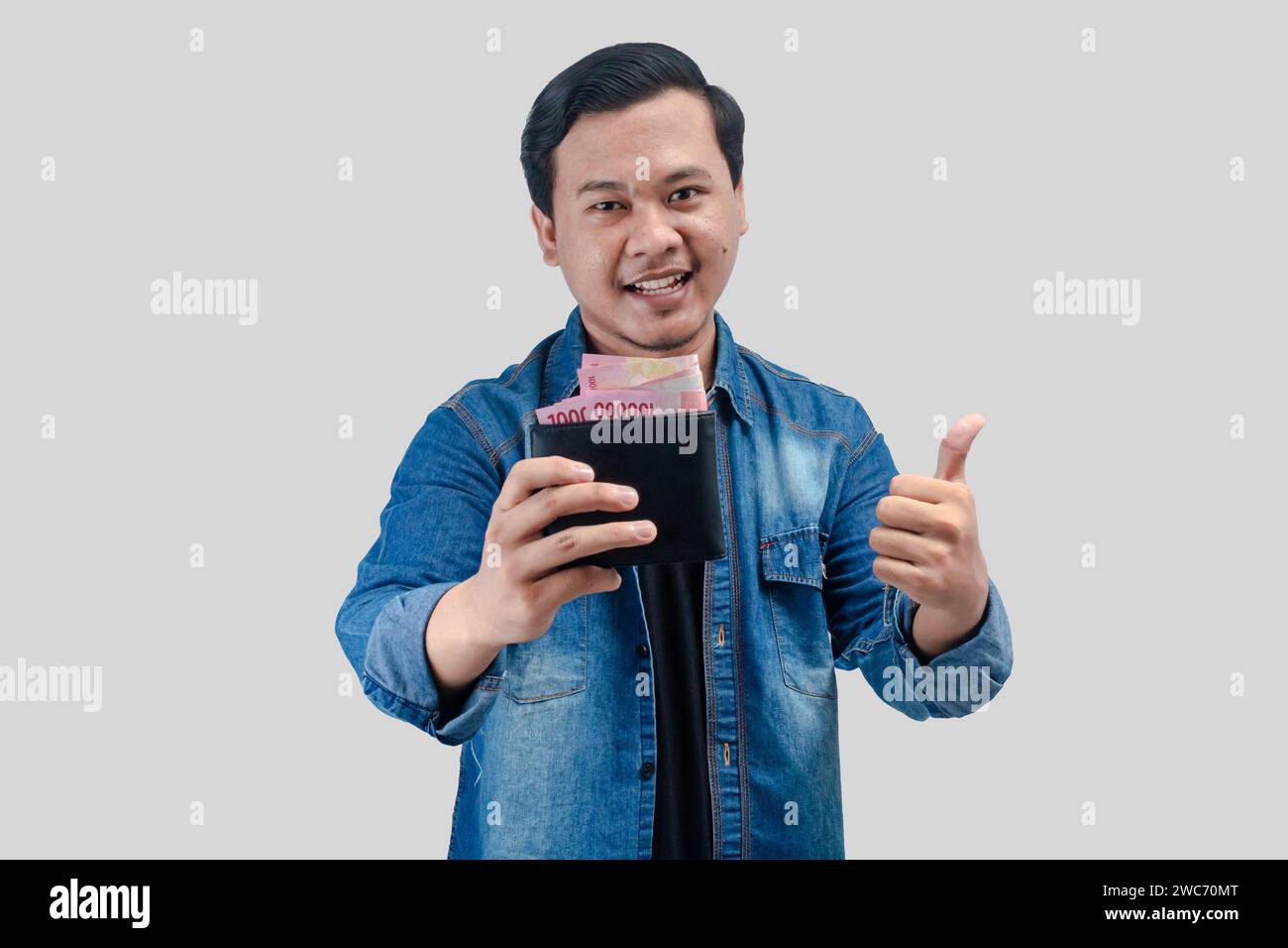 Jeune homme asiatique montrant l'expression heureuse du visage tout en tenant son portefeuille plein d'argent Banque D'Images