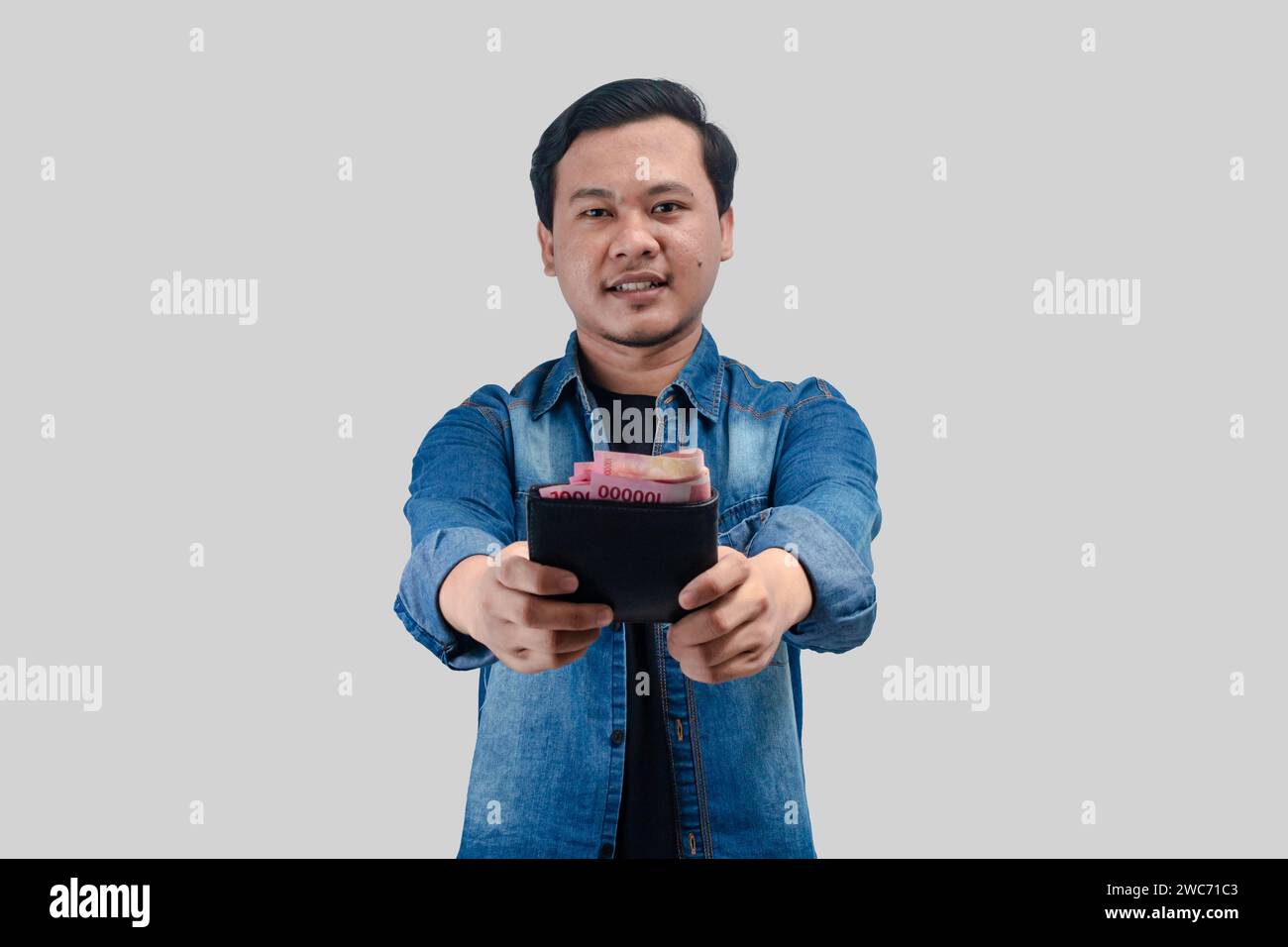 Jeune homme asiatique montrant l'expression heureuse du visage tout en tenant son portefeuille plein d'argent Banque D'Images