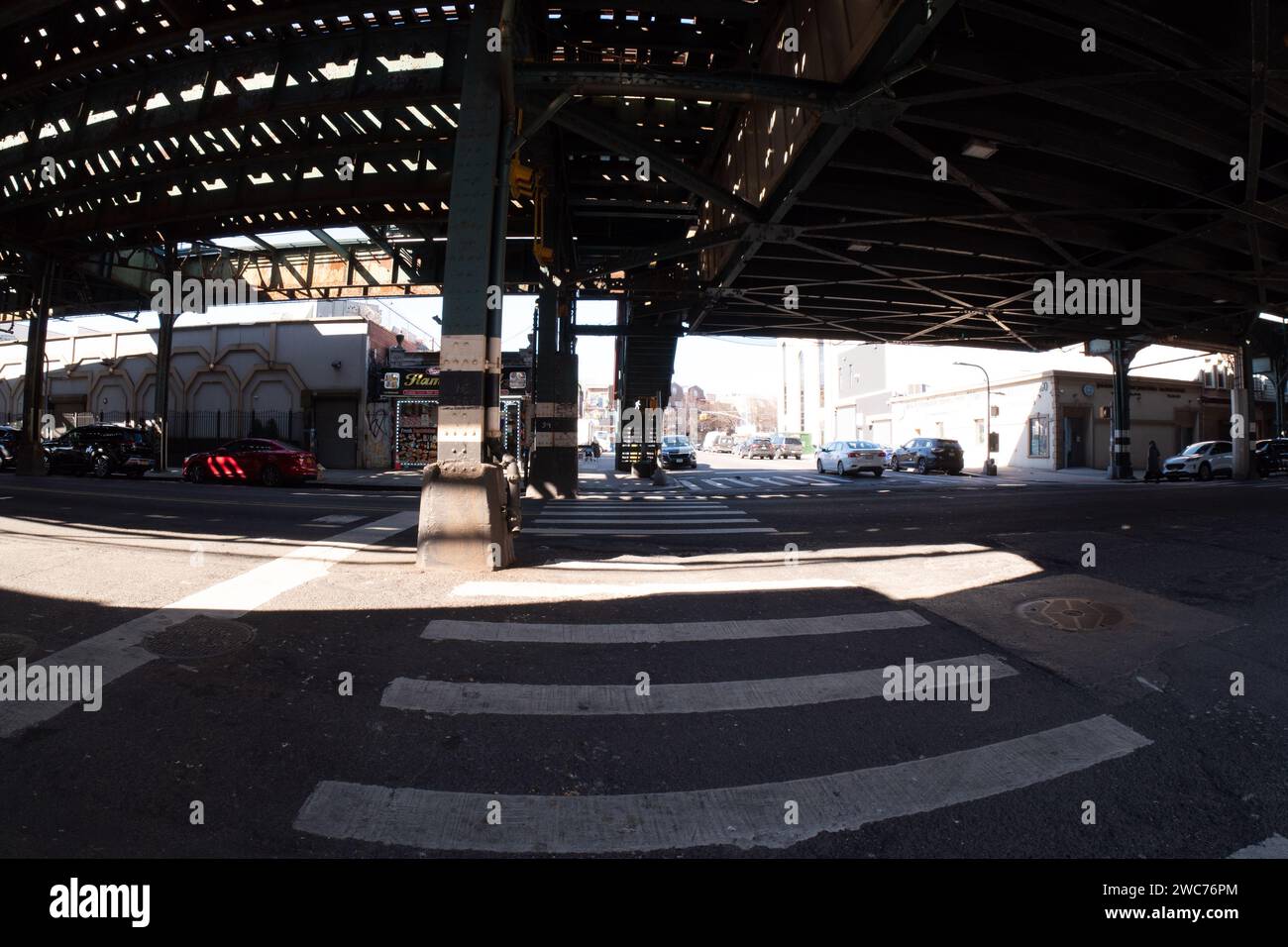 Une scène urbaine mettant en scène une rue animée sous un pont surélevé, ornée de véhicules stationnés Banque D'Images