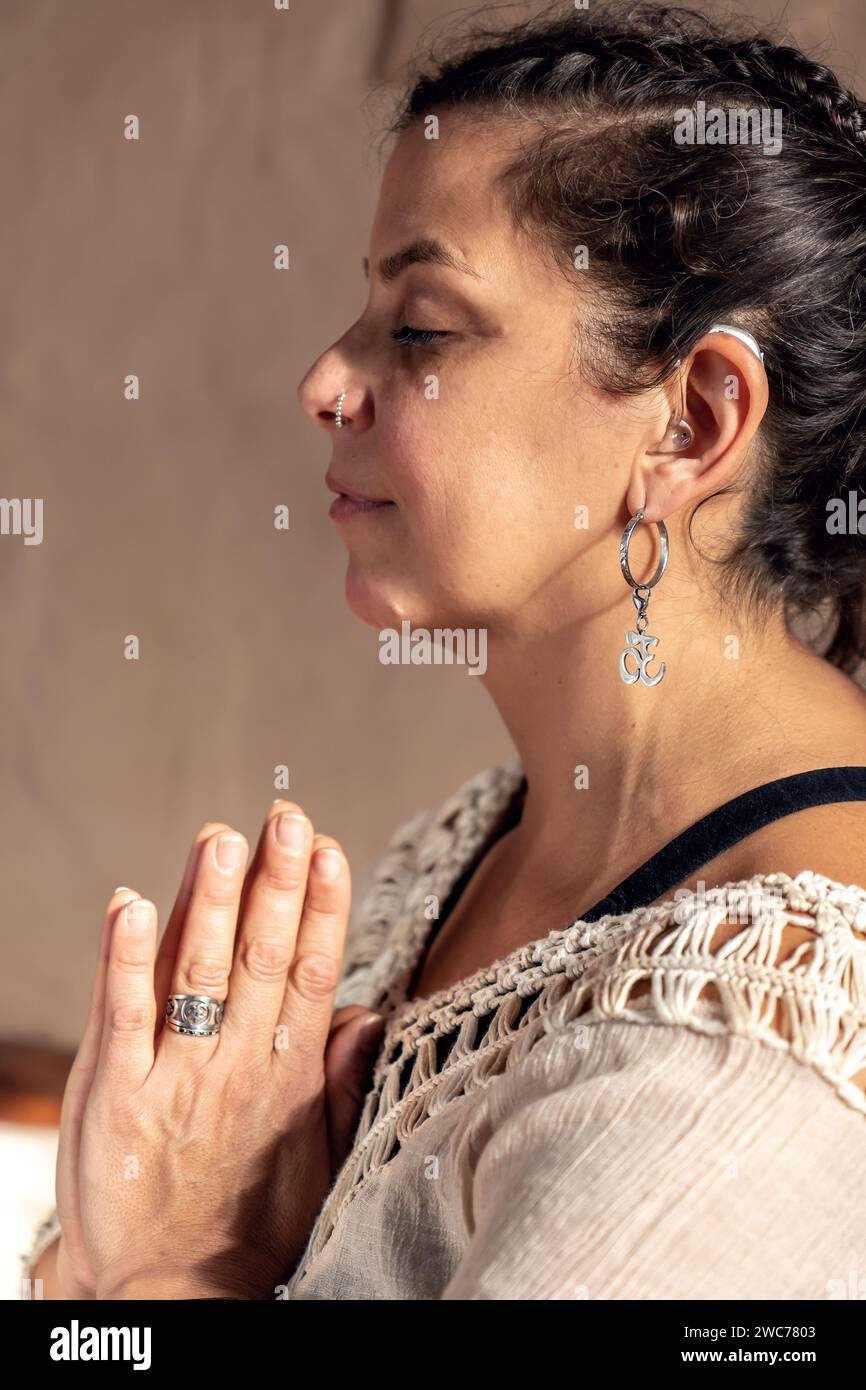 Portrait d'une femme sourde Latina profondément dans la méditation, avec ses mains serrées ensemble au niveau de la poitrine dans une pose sereine. Banque D'Images