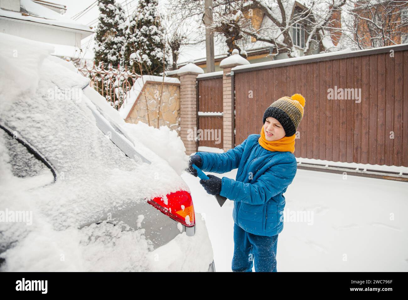 Mignon petit garçon aide son père à brosser la neige de la voiture. Déneigement de la voiture - le concept de soins de la voiture pendant l'hiver. Banque D'Images