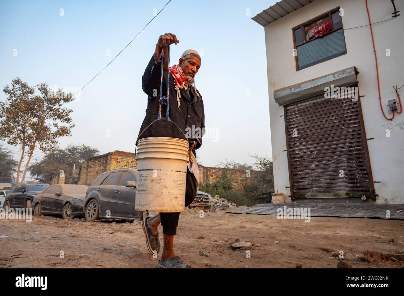 New Delhi, Inde. 14 janvier 2024. Un réfugié Rohingya rentre chez lui en transportant de l’eau potable sur un poteau tiré d’un point de distribution dans le camp de réfugiés Rohingya de Madanpur Khadar. 1 100 Rohingyas vivant dans les camps de Madanpur Khadar dépendent de l’approvisionnement en eau municipal. (Photo Pradeep Gaur/SOPA Images/Sipa USA) crédit : SIPA USA/Alamy Live News Banque D'Images