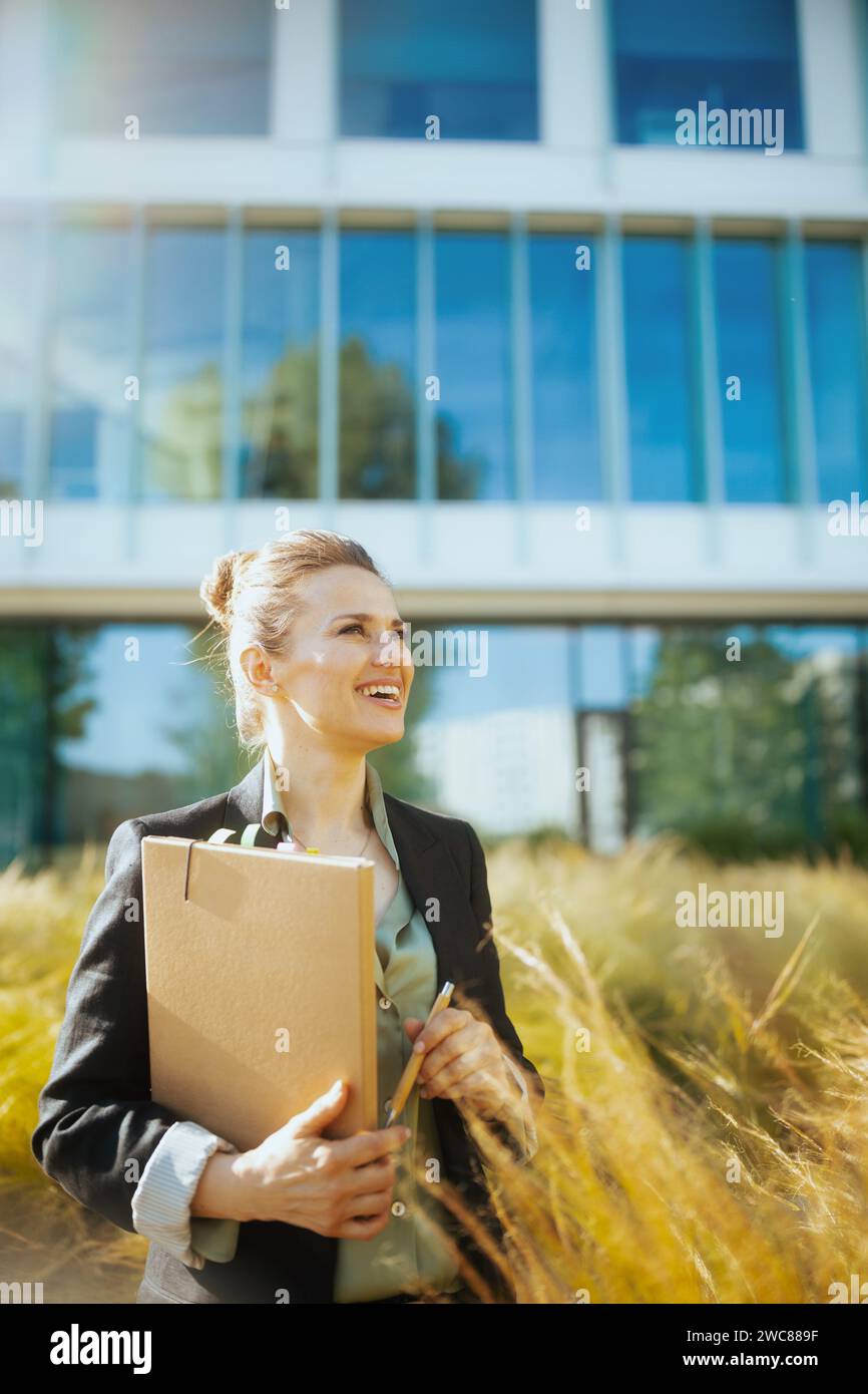 heureuse femme moderne d'âge moyen travailleur près de l'immeuble de bureaux dans la veste noire avec des documents et un dossier. Banque D'Images