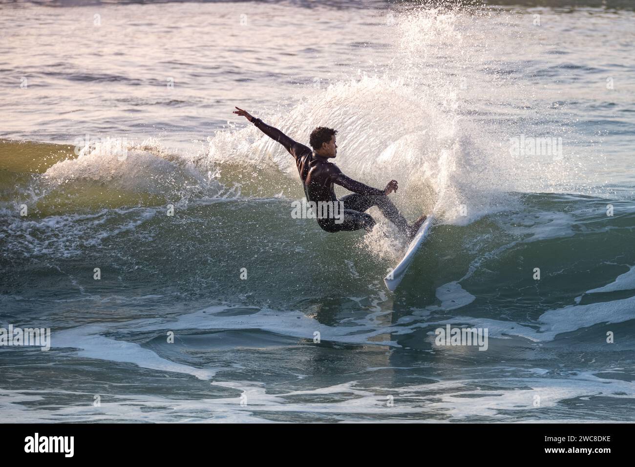 Garçon sportif chevauchant sa planche de surf sur la vague de l'océan. Banque D'Images