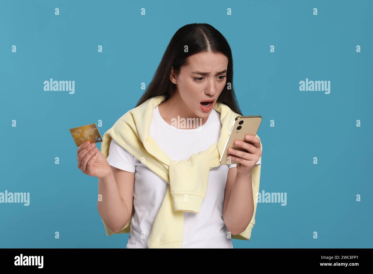 Femme choquée avec carte de crédit et smartphone sur fond bleu clair. Problème de dette Banque D'Images