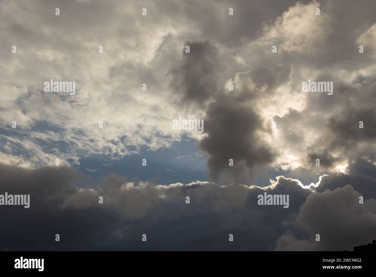 Nuages blancs et gris de pluie d'hiver avec un fond de ciel bleu. Le soleil essaie de percer les nuages comme un œil dans le ciel. Banque D'Images