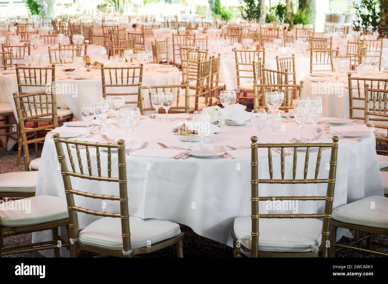 Tables rondes avec nappes blanches et verrerie servie avec chaises dorées placées à l'extérieur avant la célébration de l'événement Banque D'Images