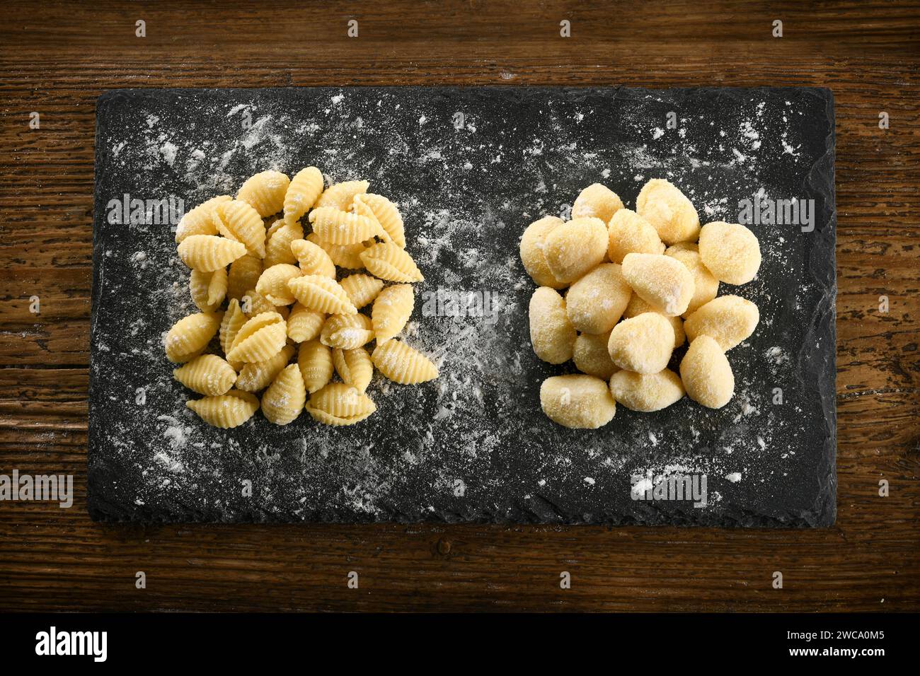 Vue de dessus de pâtes crues non cuites maison italiennes gnocchetti sardi et gnocchi placées sur un tableau noir avec de la farine Banque D'Images