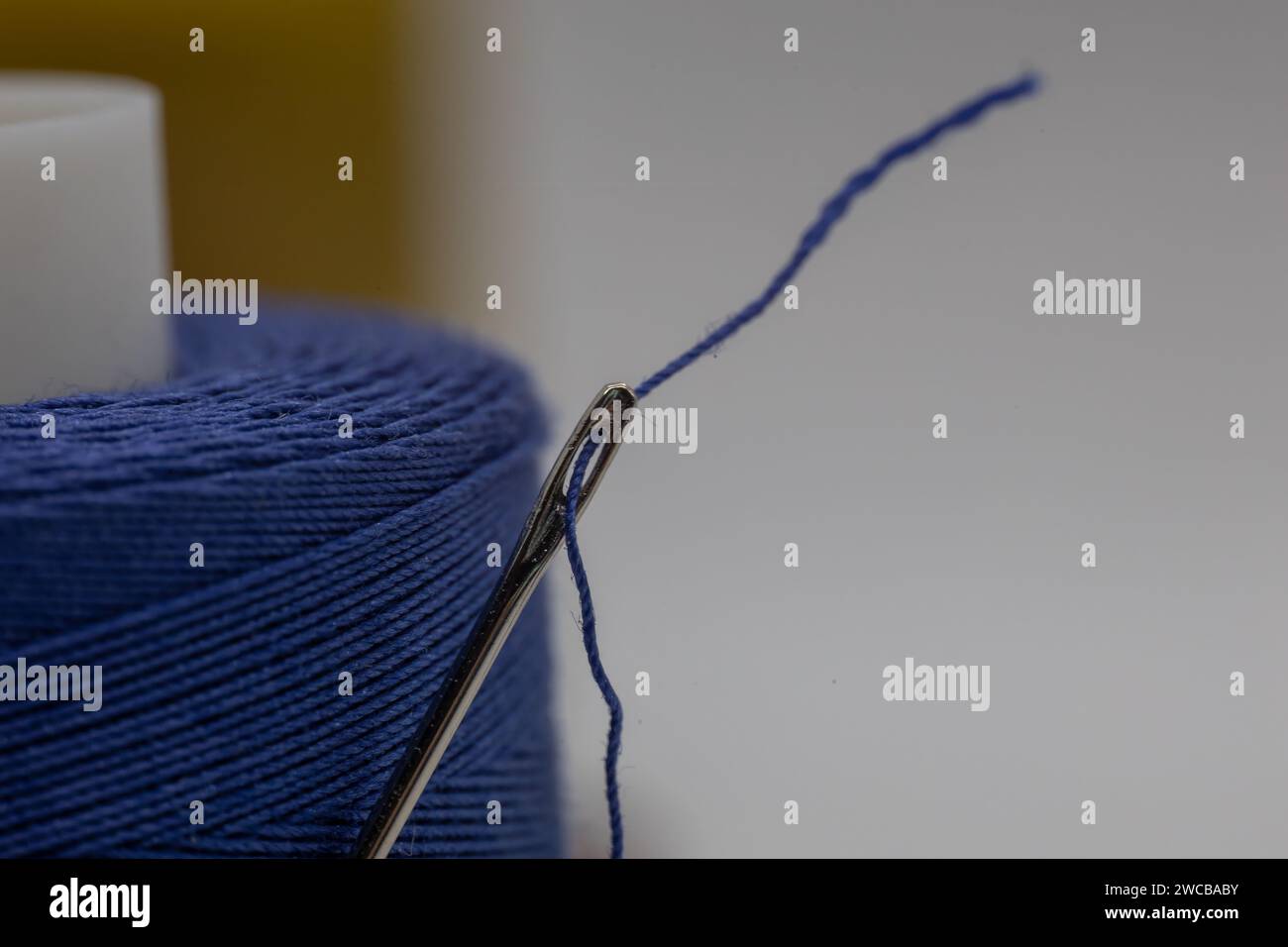 Un gros plan d'une petite aiguille dans un fil bleu sur le fond flou Banque D'Images