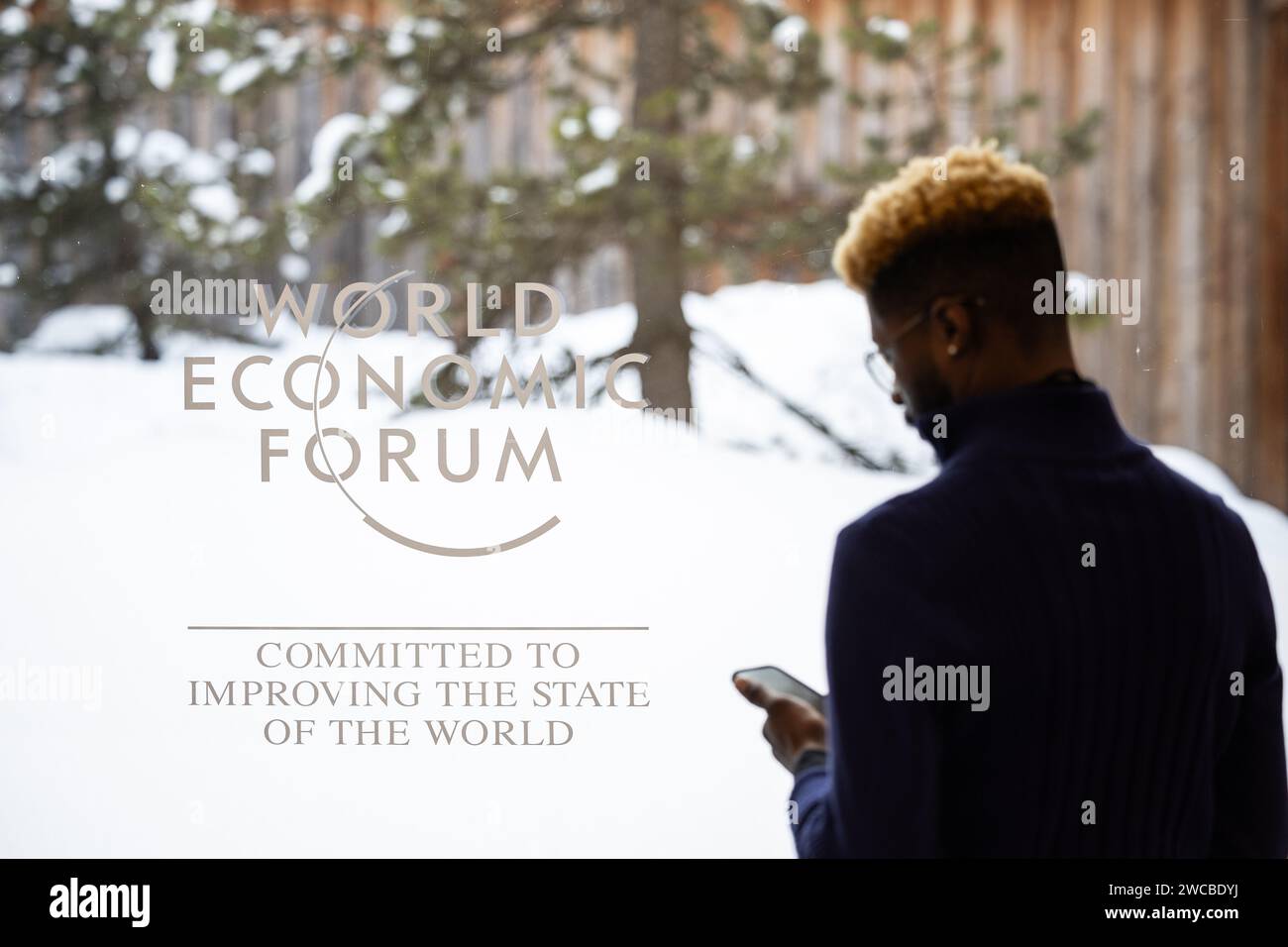 Davos, Suisse. 15 janvier 2024. Un homme se tient devant une fenêtre portant le logo du Forum économique mondial. La réunion annuelle du Forum économique mondial est considérée comme l'un des lieux de rencontre les plus importants pour les politiciens, les cadres supérieurs et les scientifiques. Le programme commence mardi. Crédit : Hannes P. Albert/dpa/Alamy Live News Banque D'Images