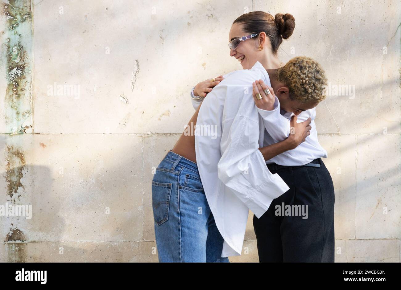 Un moment réconfortant où une jeune femme embrasse joyeusement un jeune homme par derrière, partageant tous deux un rire dans un contexte urbain. Banque D'Images