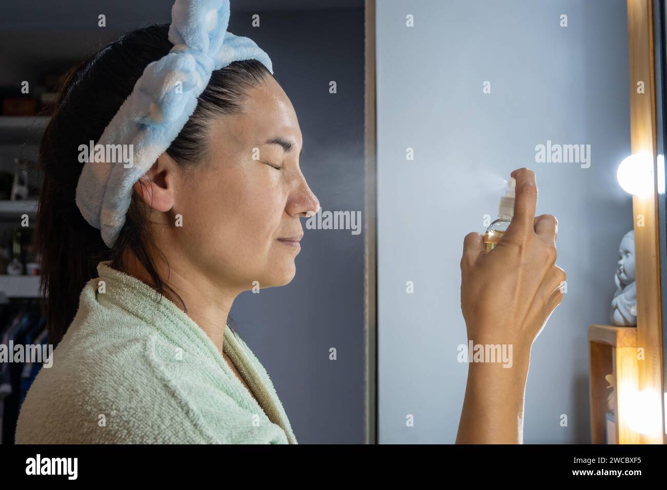 La femme applique une lotion sur son visage avec un flacon pulvérisateur. Banque D'Images