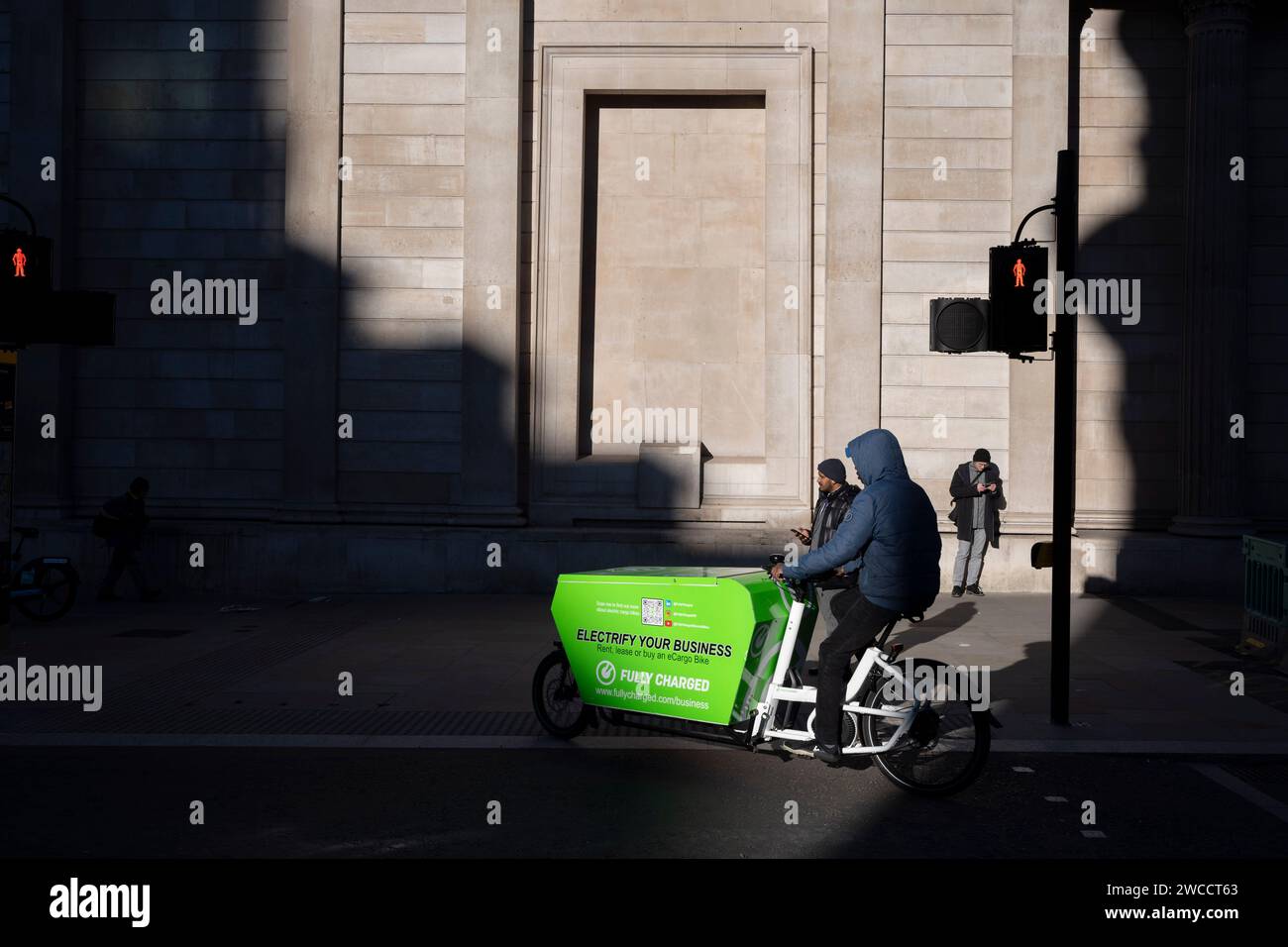 Un vélo de livraison City eCargo passe à travers la lumière du soleil hivernale sous les hauts murs de la Banque d'Angleterre sur Threadneedle Street, dans la City de Londres, le quartier financier de la capitale, le 15 janvier 2024, à Londres, en Angleterre. Banque D'Images