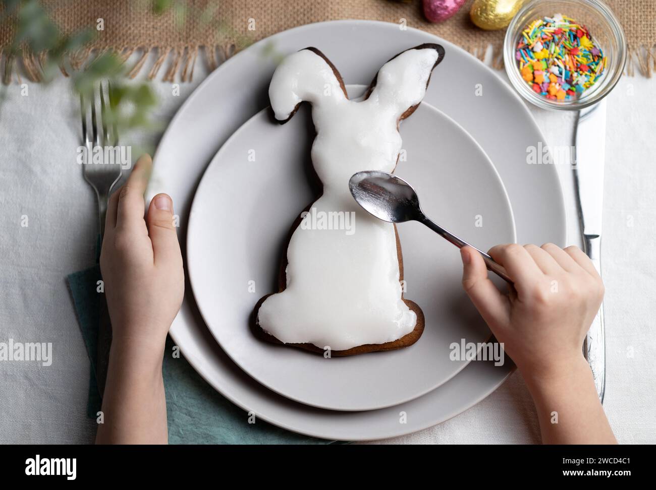 Vue de dessus d'un biscuit pain d'épice en forme de lapin. Mains d'enfant décorant biscuit avec cerise sur les vacances de Pâques Banque D'Images