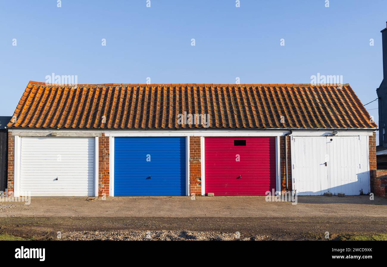 Bloc de quatre garages avec portes colorées avec un toit en tuiles. Suffolk. ROYAUME-UNI Banque D'Images