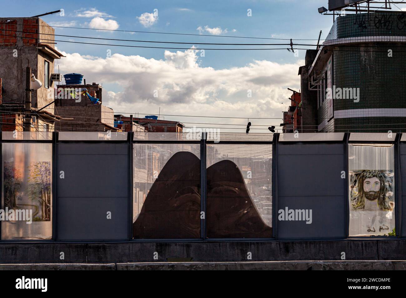 Complexo da Mare, un vaste réseau de favelas qui longe la Linha Vermelha ( ligne rouge ), l'autoroute principale de l'aéroport international de Rio de Janeiro au centre-ville - depuis 2010, la communauté est clôturée de l'autoroute par d'énormes panneaux Perspex - une barrière de séparation de 3 mètres de haut et de 7 km de long décorée de graffit (sur cette photo, une représentation des montagnes de Rio et de Jésus-Christ) - les autorités affirment qu'il fournit une barrière acoustique, les habitants la décrivent comme un «mur de la honte», une autre façon de cacher les pauvres. Banque D'Images