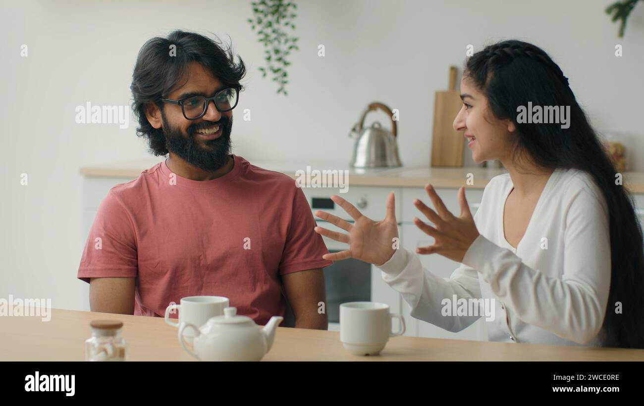 Heureux couple multiracial boire du café thé dans la cuisine à la maison bavardage amical homme arabe gars écouter histoire drôle insouciante conversation indienne femme fille Banque D'Images