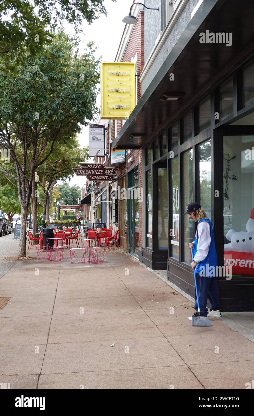 Un homme de la génération Z balayant le trottoir devant un magasin de baskets - novembre 2023 Banque D'Images