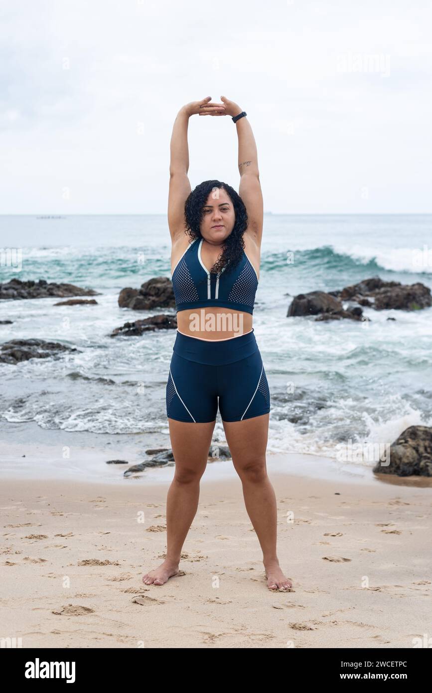 Belle jeune femme en vêtements de gym faisant des étirements sur le sable de la plage. Une vie saine. Banque D'Images