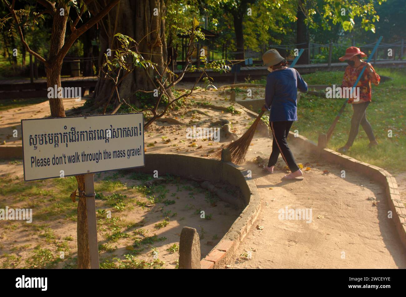 Les dames balayent des feuilles autour d'un arbre tuant dans les champs tuants du Centre génocidaire Choung EK, Phnom Penh, Cambodge. Banque D'Images