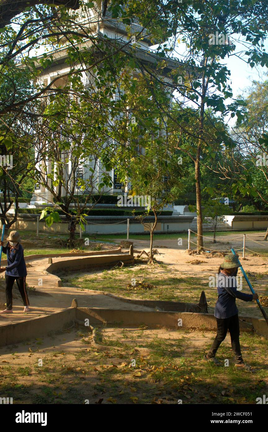 Les dames balayent des feuilles autour d'un arbre tuant dans les champs tuants du Centre génocidaire Choung EK, Phnom Penh, Cambodge. Banque D'Images