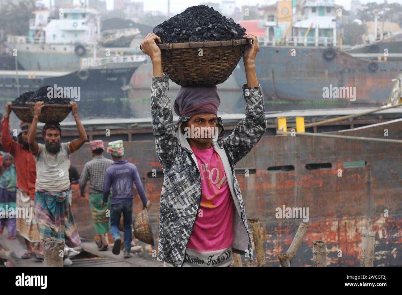 Dhaka, Bangladesh. 16 janvier 2024. Un travailleur réagit à la caméra en déchargeant un panier de charbon sur sa tête dans un marché de gros de charbon à Dhaka. (Image de crédit : © MD Mehedi Hasan/ZUMA Press Wire) USAGE ÉDITORIAL SEULEMENT! Non destiné à UN USAGE commercial ! Banque D'Images