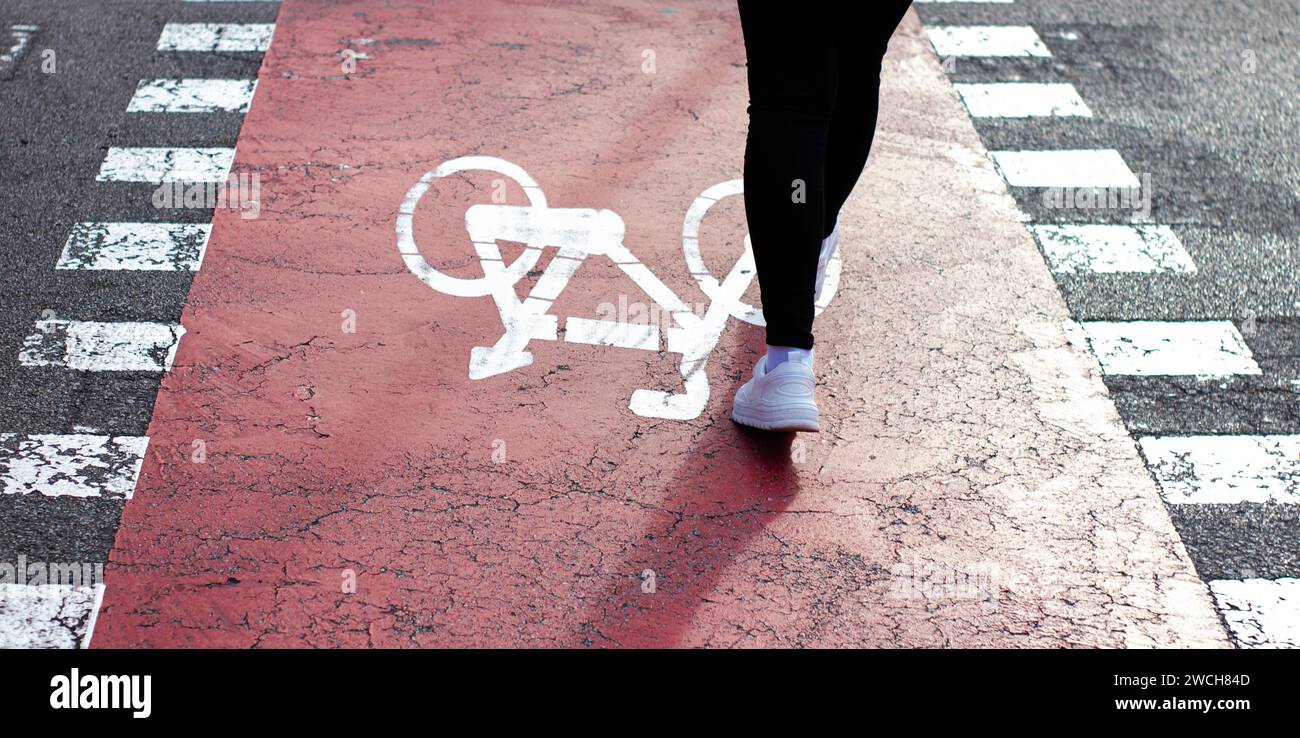 La fille en baskets blanches avec une veste en denim va traverser des piétons avec une piste cyclable. Panneau de bicyclette peint sur asphalte. Banque D'Images