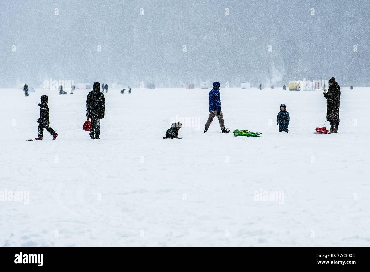 Les gens marchent et les enfants jouent avec des toboggans sur un lac gelé en hiver avec la forêt et les pêcheurs avec des tentes pêchant sur la glace sur le fond Banque D'Images