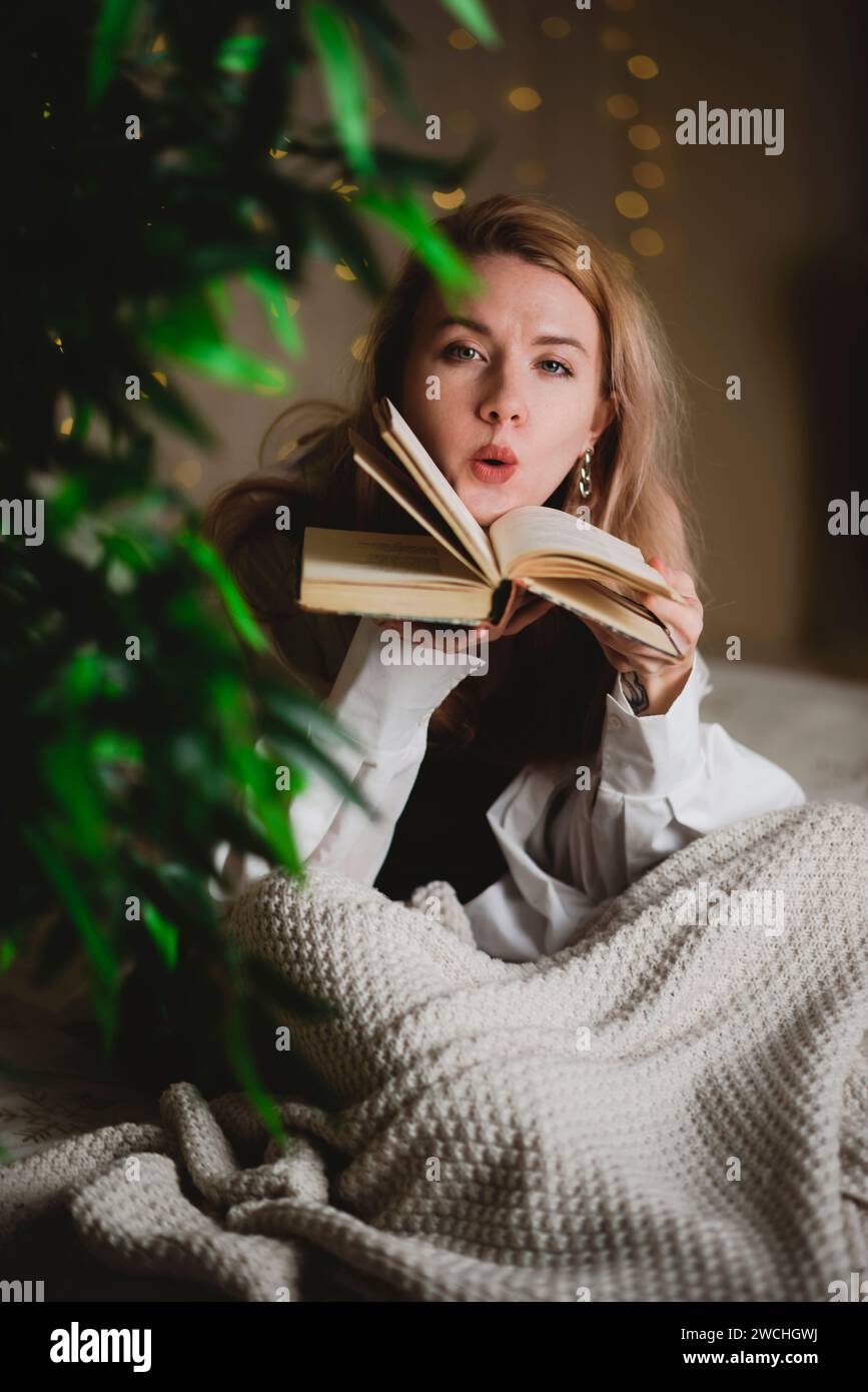 Jeune femme lisant un livre assise sur son lit à la maison la nuit Banque D'Images