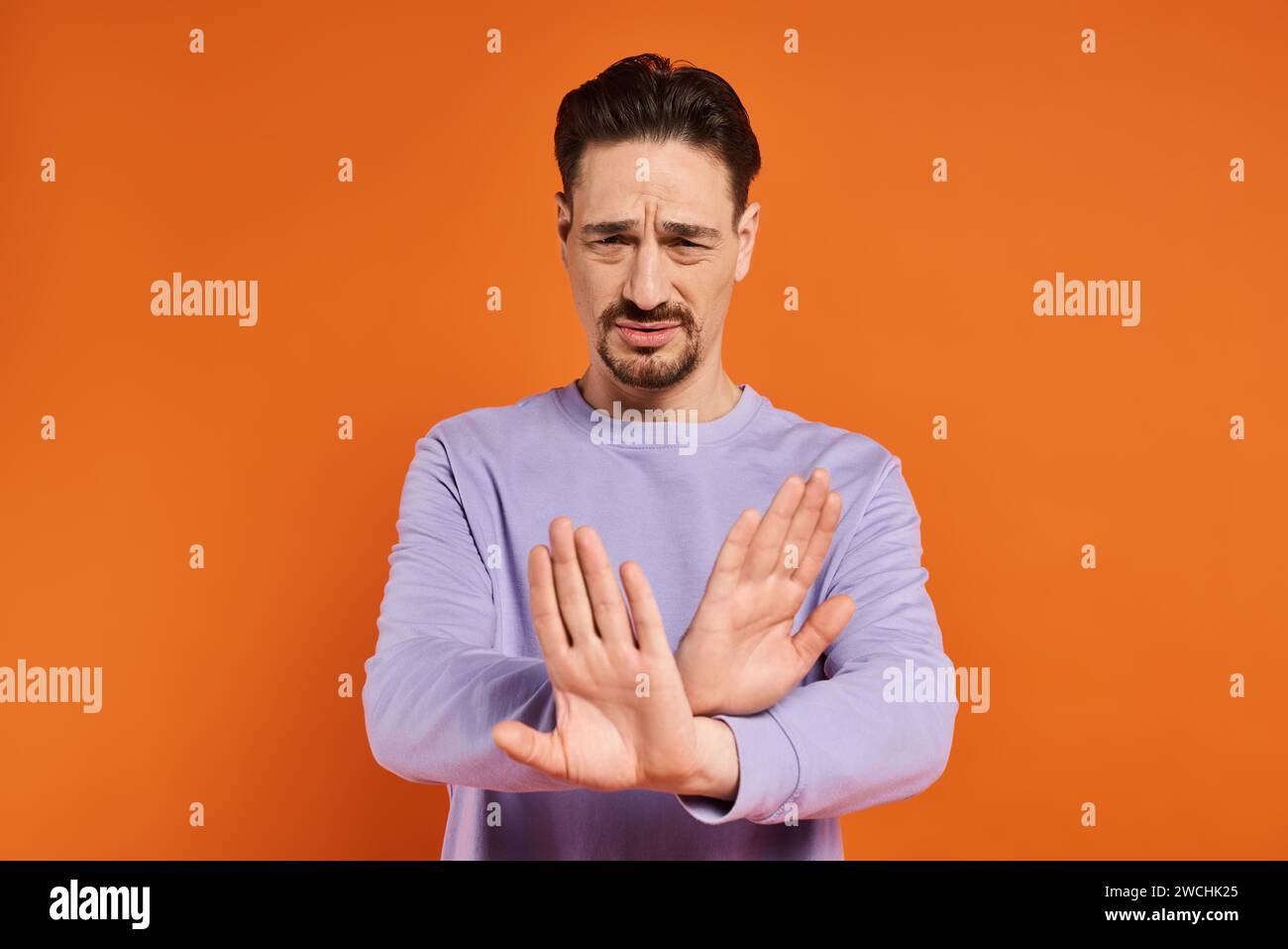 homme barbu en pull violet montrant geste de refus avec ses mains sur fond orange Banque D'Images