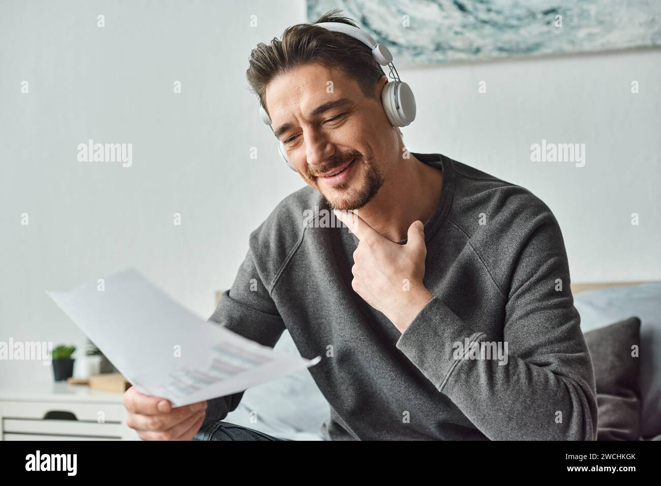 homme heureux dans des écouteurs sans fil analysant des graphiques et écoutant de la musique dans la chambre à coucher, le travail de la maison Banque D'Images