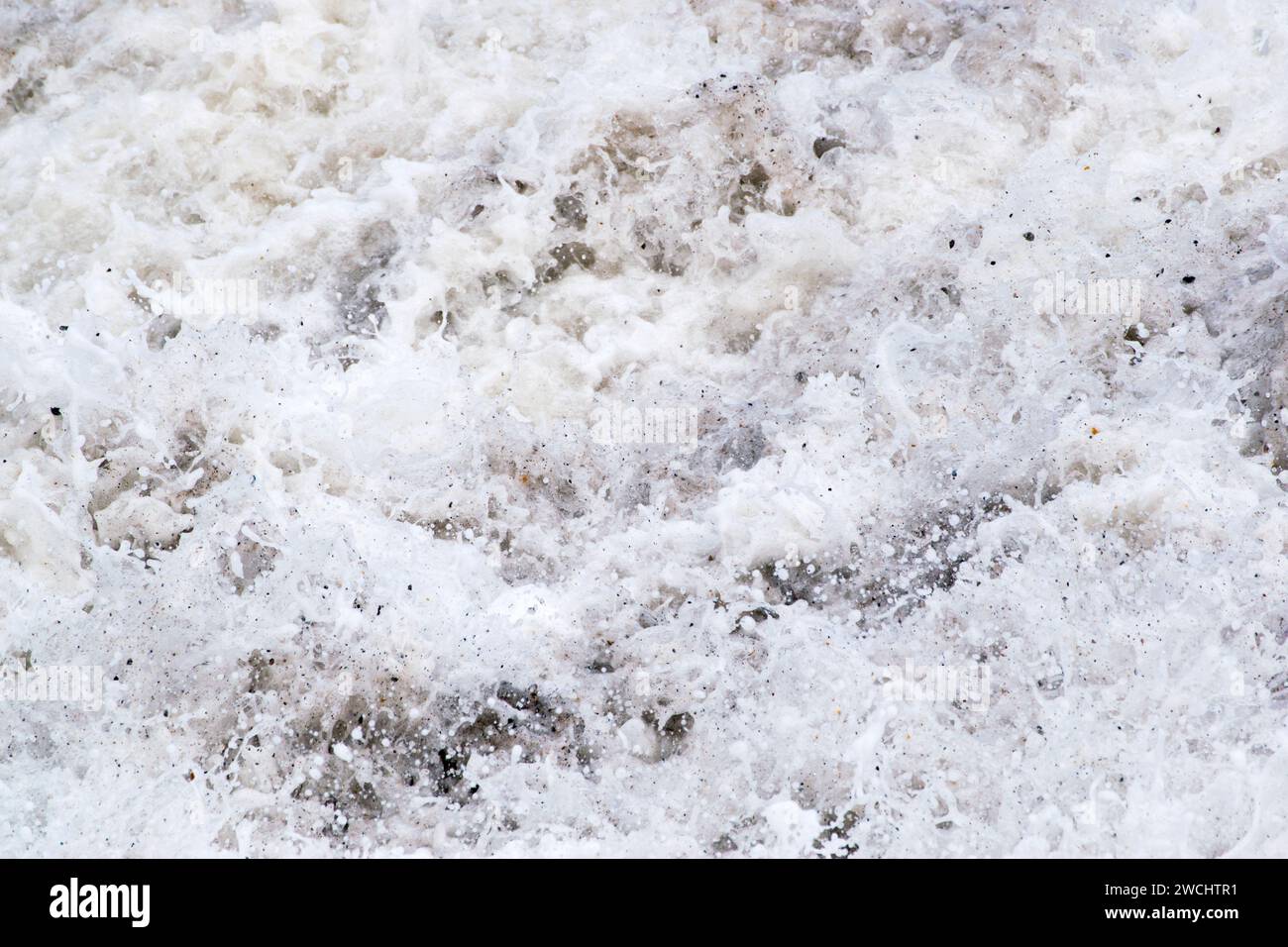 Eau de mer mousseuse, vagues atteignant le rivage, mousse de mer mélangée à des cailloux et du sable, un mouvement décrivant la photographie, presque audio, aussi. Banque D'Images