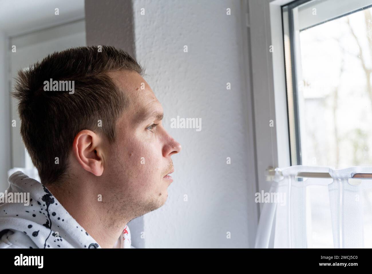 Augsbourg, Bavière, Allemagne - 14 janvier 2024 : un jeune homme regarde par la fenêtre, triste et abattu. Concept de santé mentale *** Ein junger Mann schaut traurig und niedergeschlagen aus dem Fenster. Mentale Gesundheit Konzept Banque D'Images