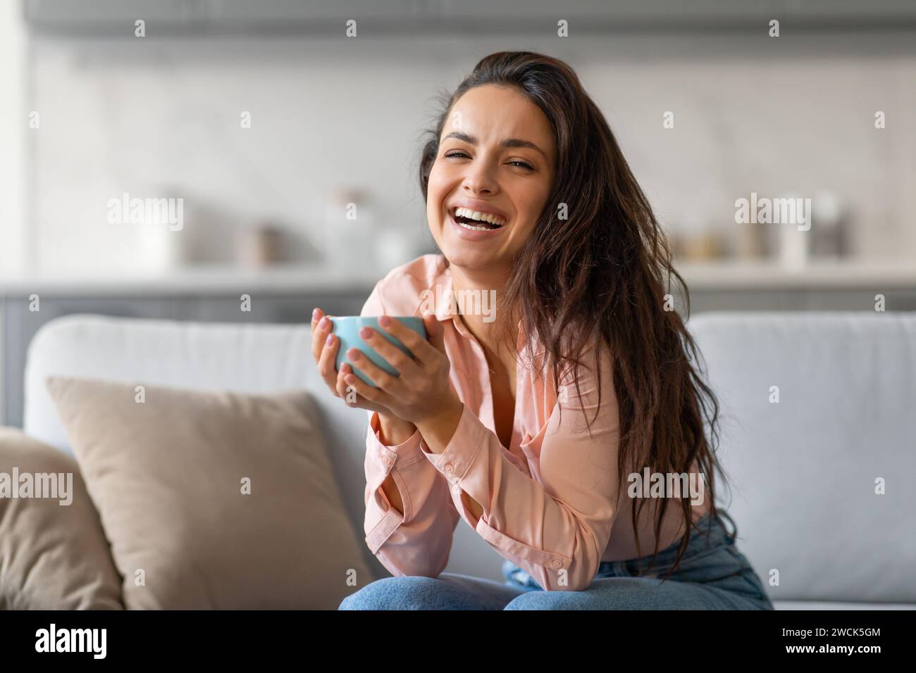 Femme joyeuse riant tout en tenant la tasse, dans un cadre confortable à la maison Banque D'Images