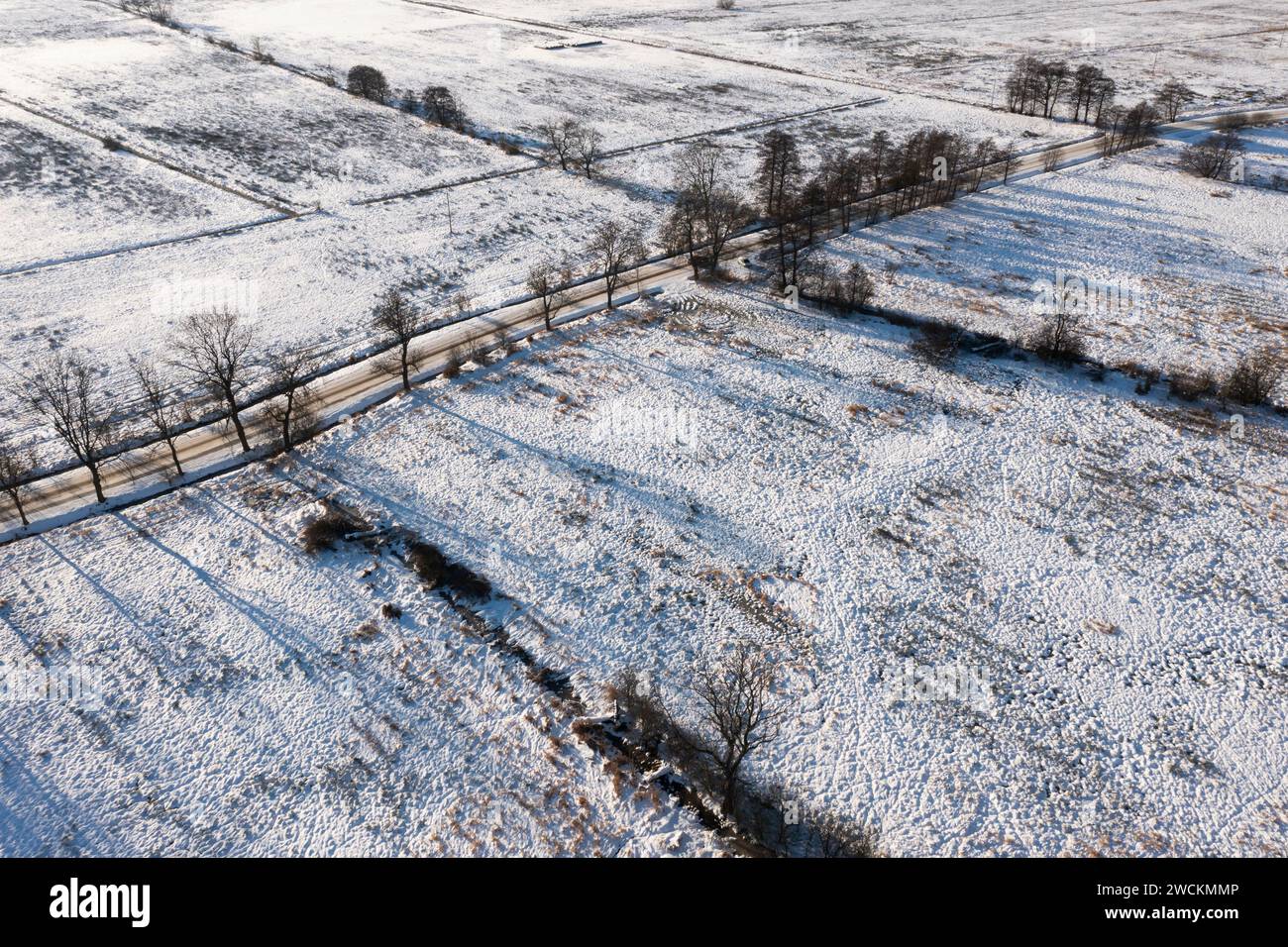 Une route couverte de neige entre champs et prairies, vue depuis un drone. Banque D'Images
