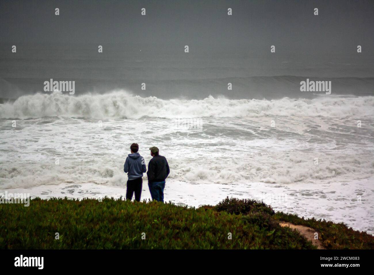 Deux hommes regardent d'énormes vagues de tempête hivernale au large des côtes de Californie Banque D'Images