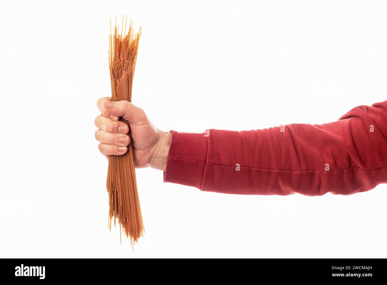 La main d'un homme dans un chandail rouge tenant un ensemble de spaghettis sur un fond blanc. Glucides et pâtes de blé entier dans l'alimentation Banque D'Images