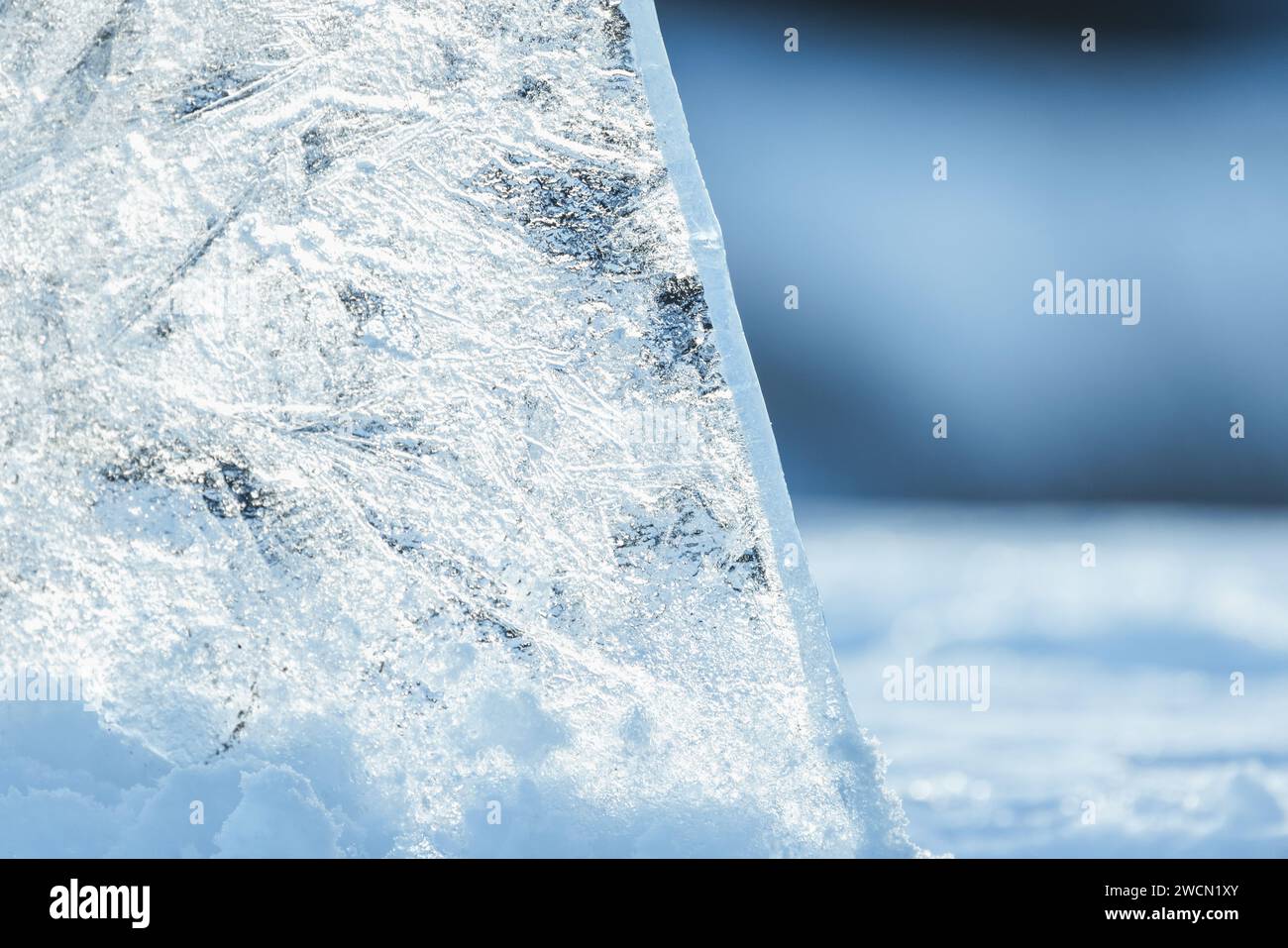 Un éclat de glace transparent se tient dans une dérive de neige lors d'une journée ensoleillée d'hiver, photo en gros plan avec flou sélectif Banque D'Images