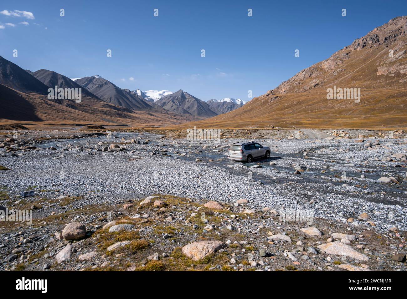 Véhicule hors route traversant une rivière dans la vallée de Burkhan, paysage montagneux avec des sommets glaciaires et des prairies dorées, Terskey Ala-Too, Tien Shan Banque D'Images