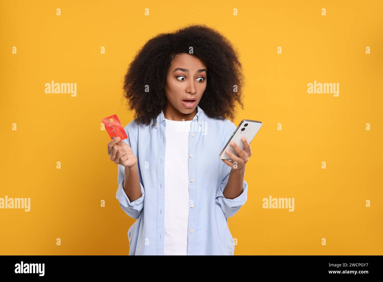Femme choquée avec carte de crédit et smartphone sur fond orange. Problème de dette Banque D'Images