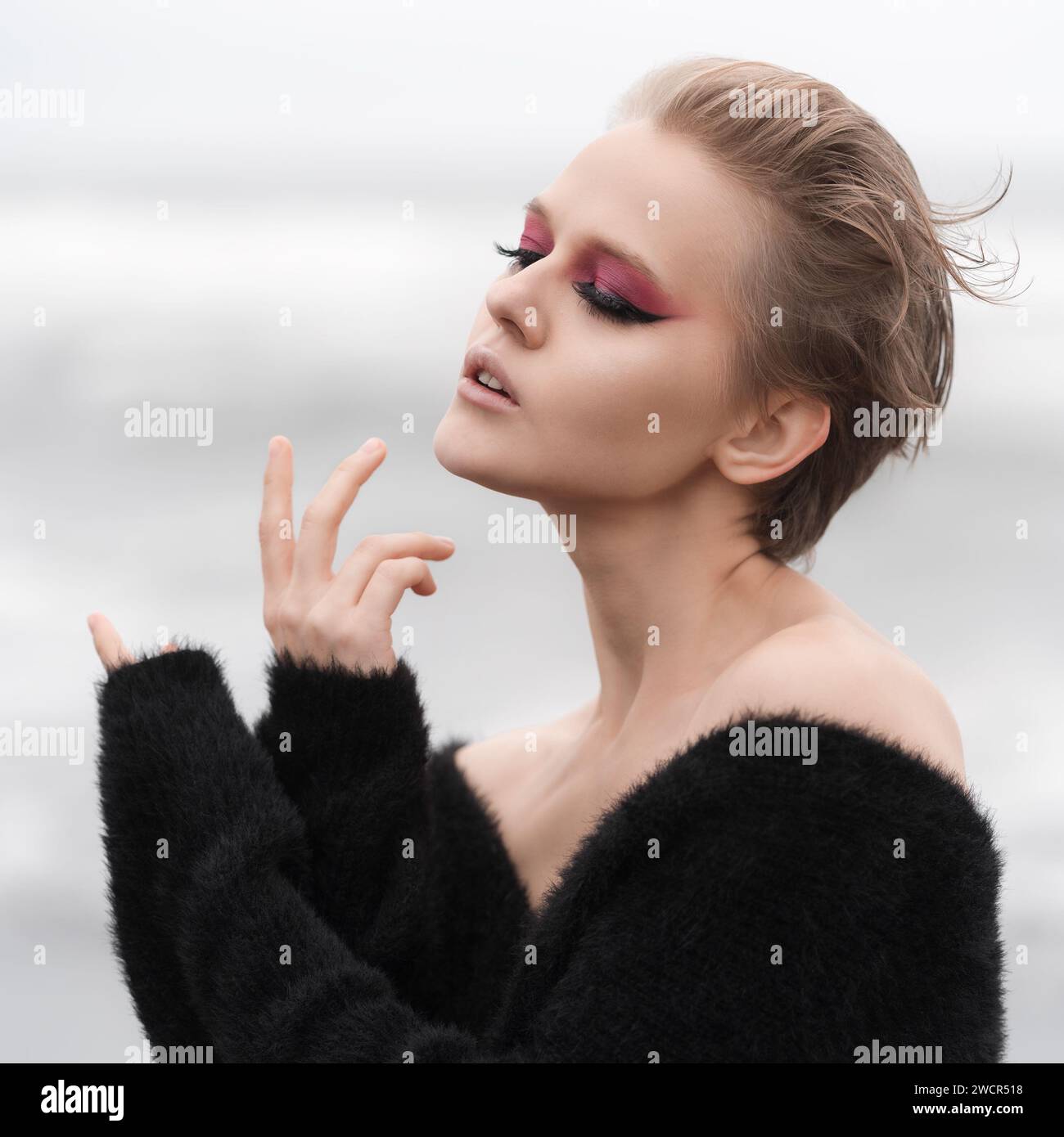 Portrait de femme blonde les yeux fermés. Modèle de mode avec maquillage lumineux et cheveux courts posant à l'extérieur sur fond naturel blanc Banque D'Images