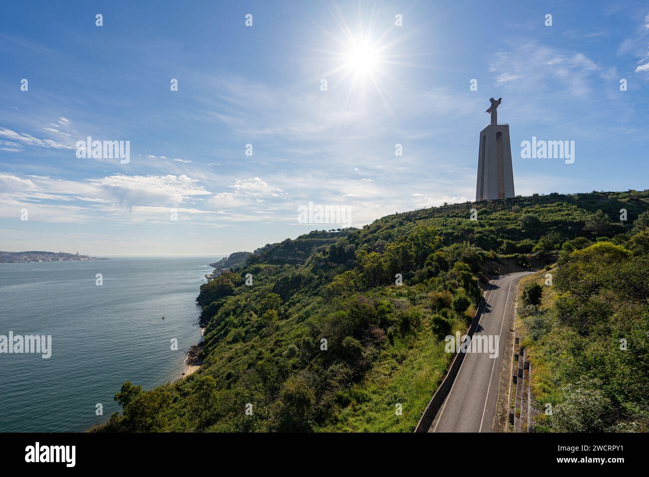 Statue du Christ à Almada/Lisbonne, avec le soleil du matin tombant sur la route goudronnée et le Tage Banque D'Images