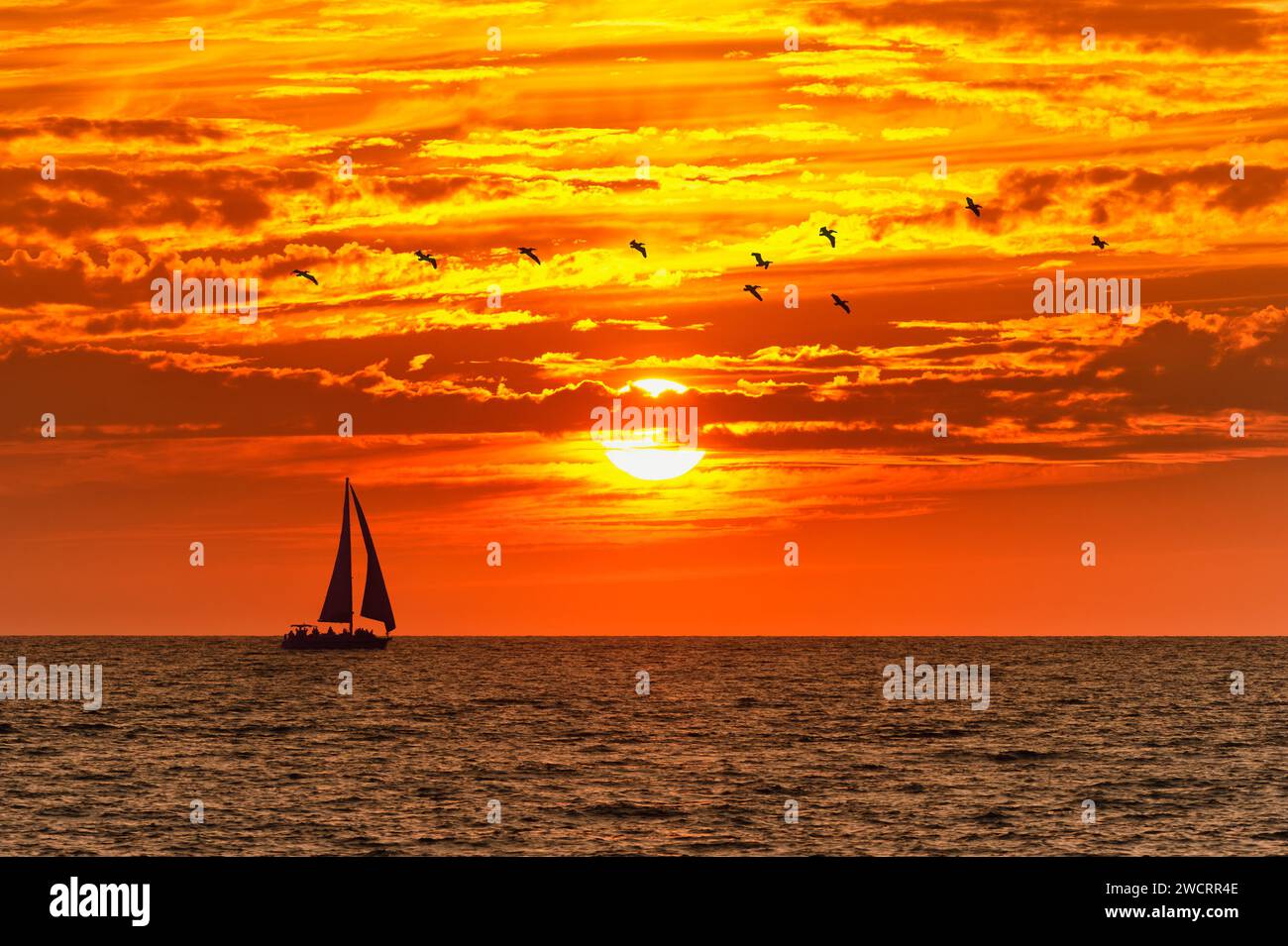 Un beau coucher de soleil sur l'océan avec Une vague se brisant sur la rive et un Voilier en voilier sur Horizon Banque D'Images